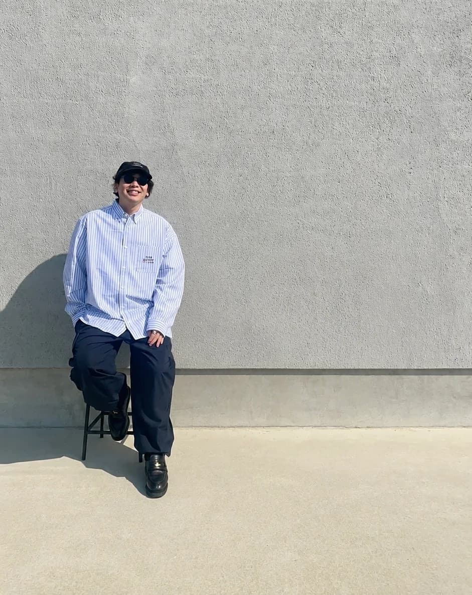 コンクリートの壁を背景にスツールへ腰かける、SEWN.TOKYO 創業者 Kaito Nishimura。